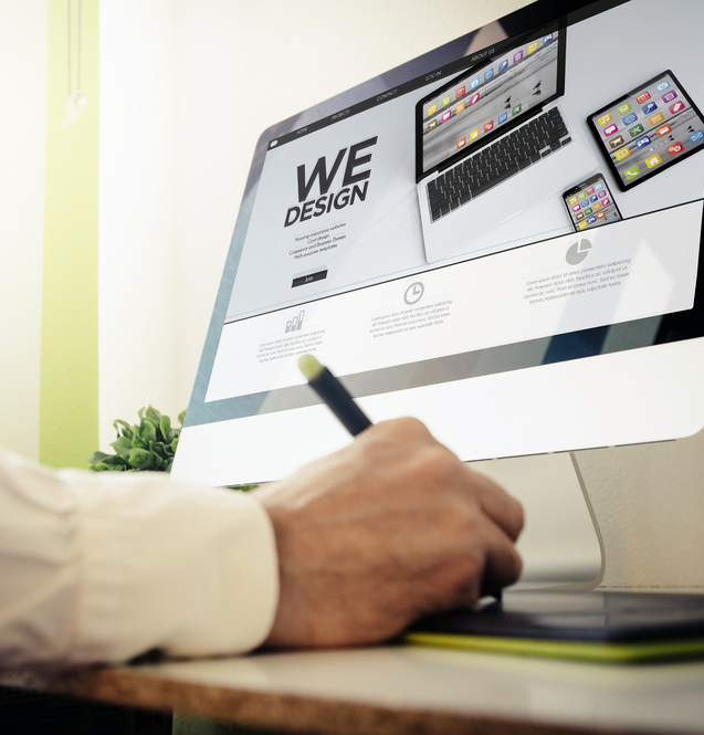 Workspace featuring a hand writing on a tablet beside a computer displaying a design website.